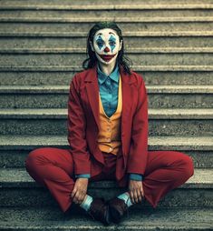 a man dressed as the joker sitting on steps with his face painted like a clown