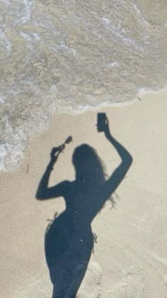 a shadow of a woman on the beach with a cell phone in her hand,