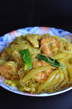 a bowl filled with noodles and shrimp on top of a black table next to a fork