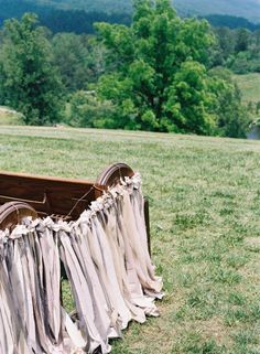 an old wooden box with clothes hanging from it's sides on the grass in front of mountains