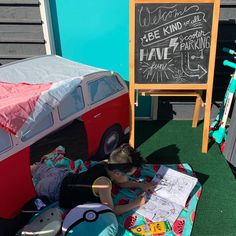 a little boy laying on top of a blanket next to a chalkboard sign and van