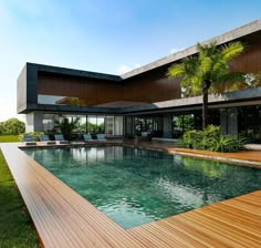 an empty swimming pool in front of a modern house with wooden decking and large windows