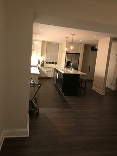 an empty kitchen and dining room with dark wood flooring, white cabinets and counter tops