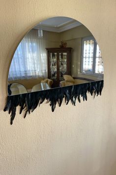 a mirror hanging on the side of a wall with black feathers attached to it's sides