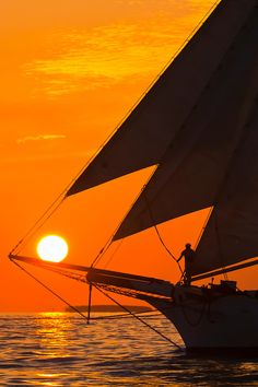 the sun is setting behind a sailboat in the ocean with it's sails down