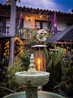 an outdoor fountain in front of a building with flowers and plants on the outside wall