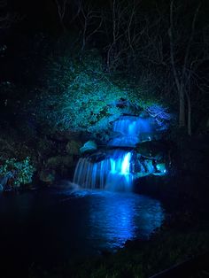 a small waterfall lit up at night with blue lights in the water and trees around it