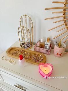 a wooden tray with jewelry on top of a white dresser next to a candle and other items