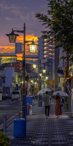 two people walking down the street with umbrellas in their hands at sunset or dawn