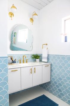 a bathroom with blue and white tiles on the walls, gold faucets and a large round mirror