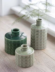 two green vases sitting on top of a wooden floor next to a window sill