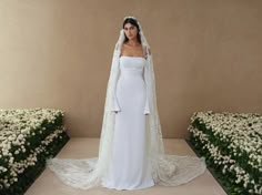 a woman in a white wedding gown and veil standing next to some flowered bushes