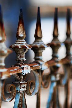 an old iron fence with rusted metal posts and finials on the top, in front of a blurred background