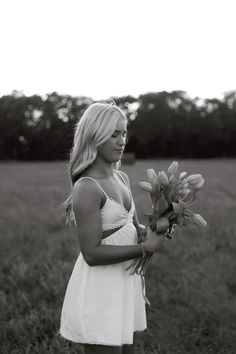 black and white photograph of a woman in a field holding flowers with one hand, looking at the camera