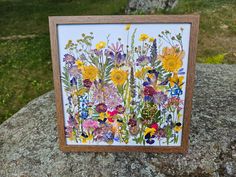 a wooden frame with flowers on it sitting on top of a large rock in the grass