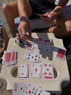 a man sitting on a beach next to a table with playing cards in front of him