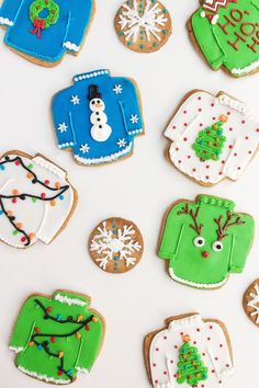 decorated cookies are arranged on a white surface with snowmen, sweaters and trees