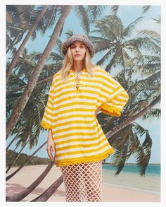 a woman standing on the beach wearing a yellow and white striped dress with fishnet stockings