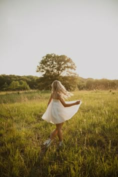 a woman in a white dress is walking through the grass with her back to the camera