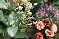 a bunch of flowers that are sitting on a table with green leaves and purple flowers