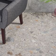 a grey chair sitting on top of a floor next to a potted green plant