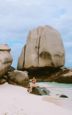 a woman standing on top of a sandy beach next to large rocks