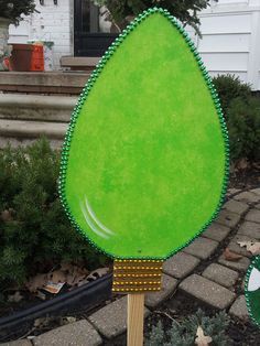 a large green tree shaped object sitting on top of a wooden stick in front of a house