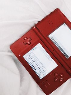 a red nintendo wii game console sitting on top of a bed next to a white sheet