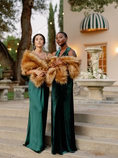 two women in long dresses standing on steps with fur stolers around their shoulders and arms