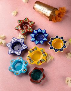 colorful ceramic bowls and vases sitting on a pink surface with petals scattered around them