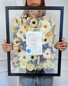 a woman holding up a frame with flowers on it