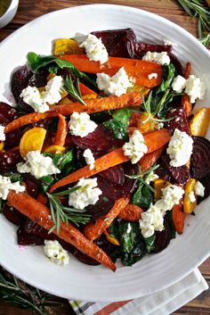 a white plate topped with carrots, beets and feta on top of a wooden table