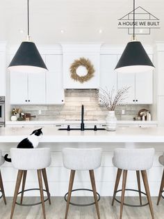 a kitchen with four stools and three lights over the island in front of it