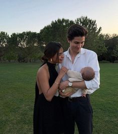 a man and woman holding a baby in their arms while standing on top of a lush green field