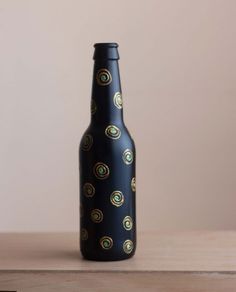 a black bottle with gold circles on it sitting on a wooden table next to a brown wall