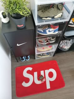 a red rug with the word sup on it next to some shoes and plants