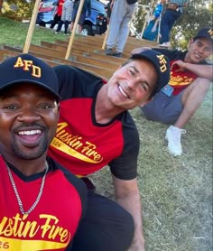 two men in matching shirts posing for a photo with other people behind them on the grass