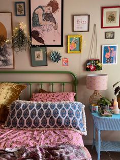 a bedroom with pictures on the wall and a bed covered in pink sheets, pillows and blankets