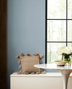 a room with blue walls, white furniture and flowers in vases on the window sill