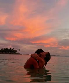 two people are kissing in the water with pink and blue skies behind them at sunset