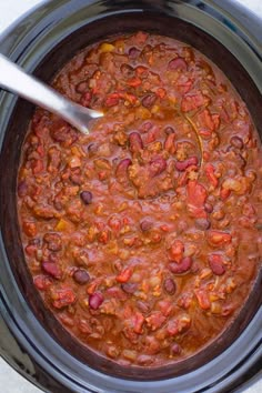 a spoon is in a slow cooker filled with chili beans and meats, ready to be cooked