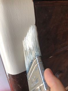 a person holding a paintbrush in their hand and painting the side of a cabinet