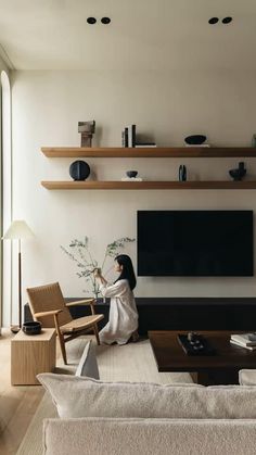 a woman sitting on the floor in front of a flat screen tv with shelves above her