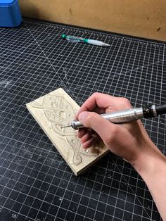 a person using a pen to write on a piece of wood with a carving tool