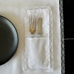 a black plate and silverware sitting on top of a white table cloth with lace