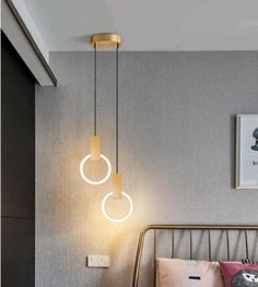 two circular lights hanging from the ceiling above a bed in a room with grey walls