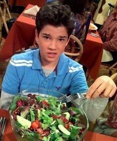 a boy sitting at a table with a salad in front of him