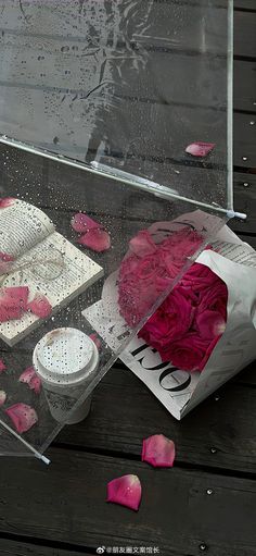 pink roses are in a clear box on a wooden table with petals scattered around it