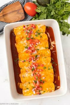 an enchilada in a white casserole dish next to tomatoes and parsley