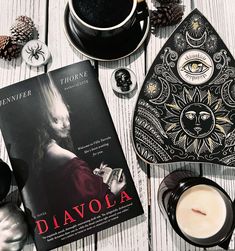 a book, candle, and other items on a white wooden table with pine cones